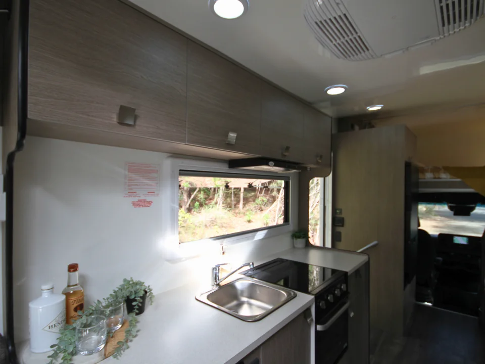 Saxby F-2 interior — kitchen bench with stainless sink, 3-burner cooktop, rangehood and overhead cabinets