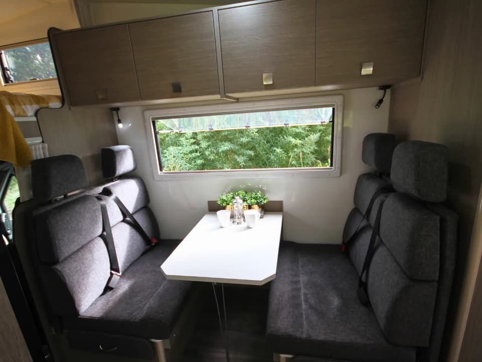 Saxby F-2 demo interior — rear dinette with facing bench seats, seatbelts and overhead storage