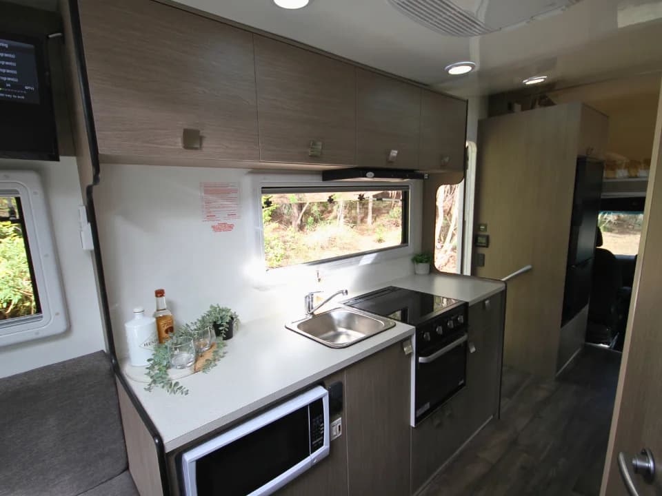 Saxby F-2 demo interior — kitchen bench close-up with stainless sink, 3-burner cooktop and microwave