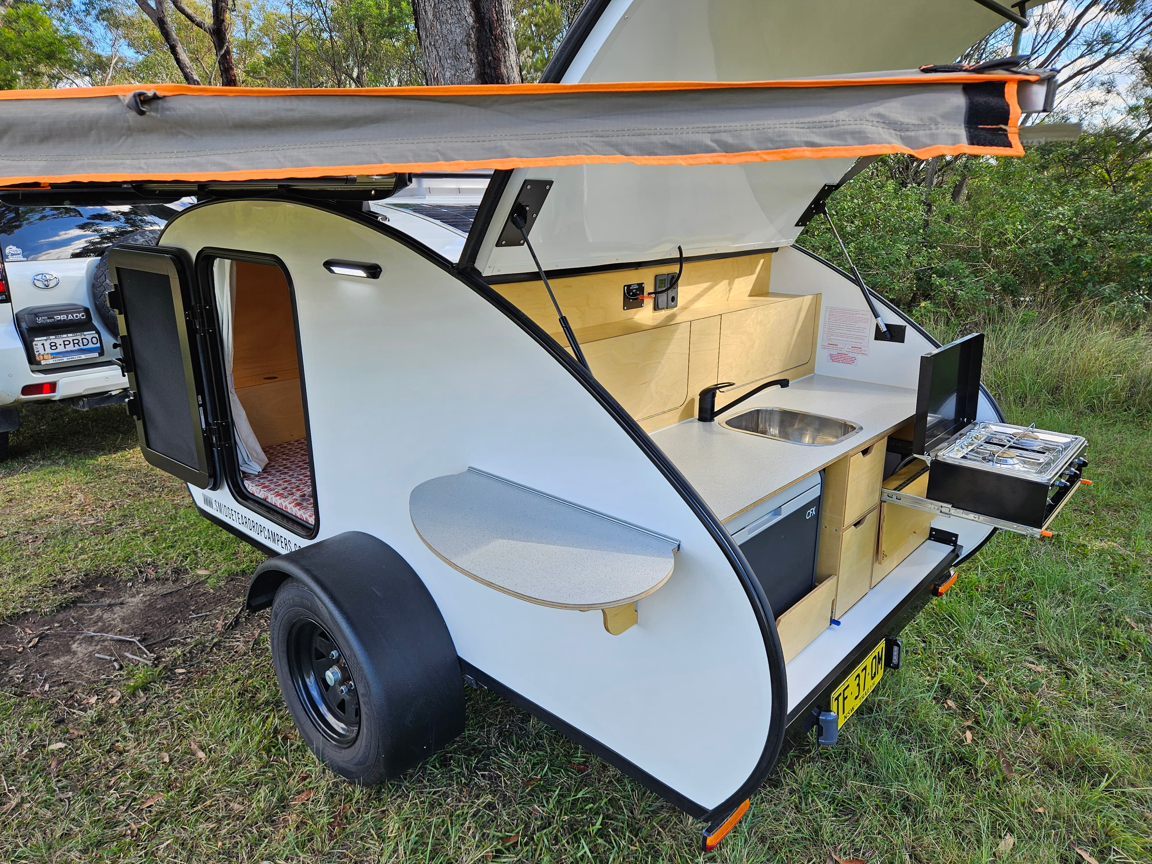 2024 Smidge Breeze — awning deployed and rear galley open showing stainless sink and laminate benchtop