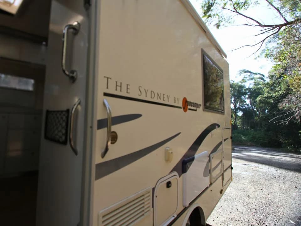 2011 Suncamper Sydney motorhome — driver's side entry door open showing The Sydney by Suncamper badge
